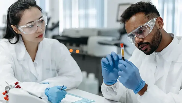 Two scientists carefully study a vial containing a blood sample.
